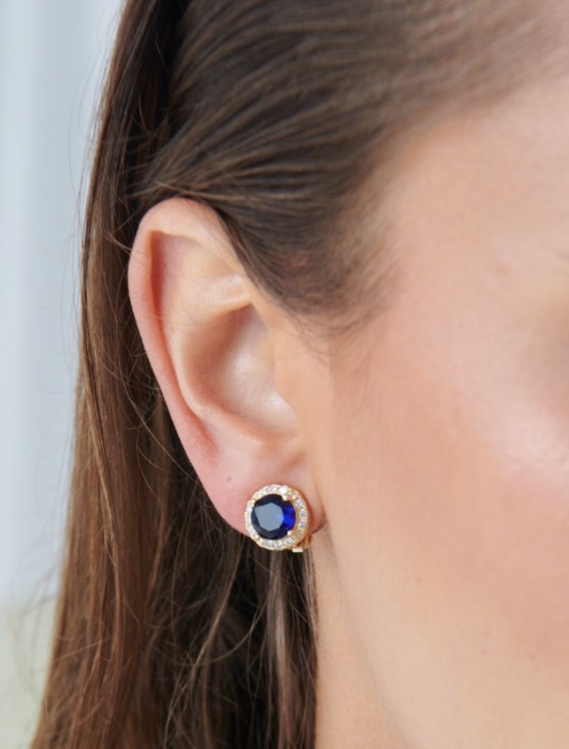 model wearing gold clip on earring with small dark blue stone surrounded by white crystals - zjoosh